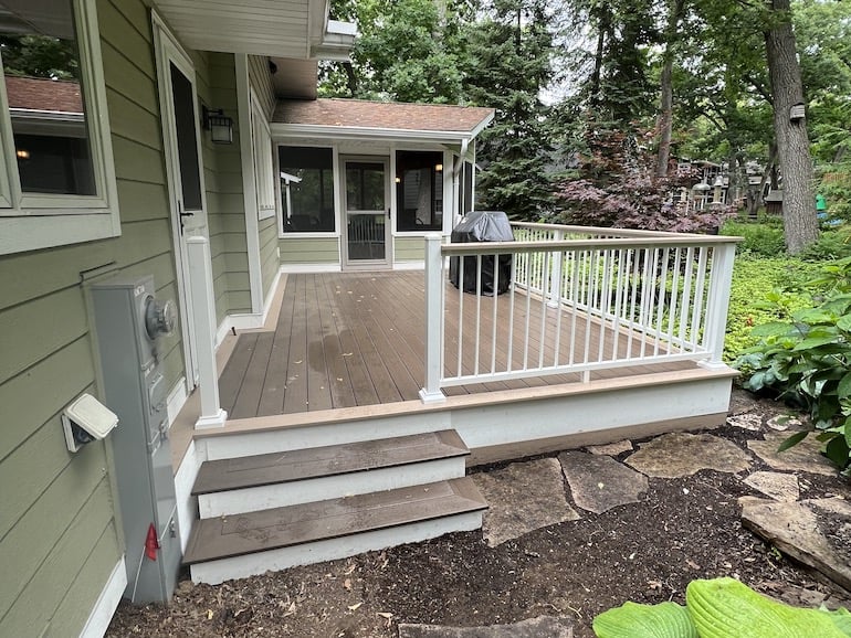 Light brown deck with white stair risers & fascia along with white aluminum railings attached to a light sage home.